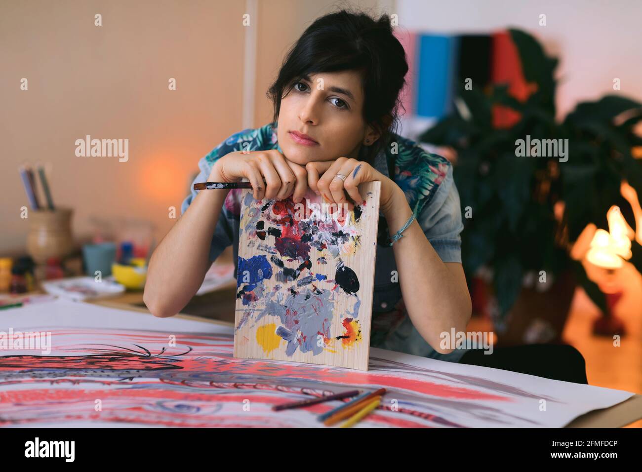 Portrait of female artist with paint brush and palette in studio ...