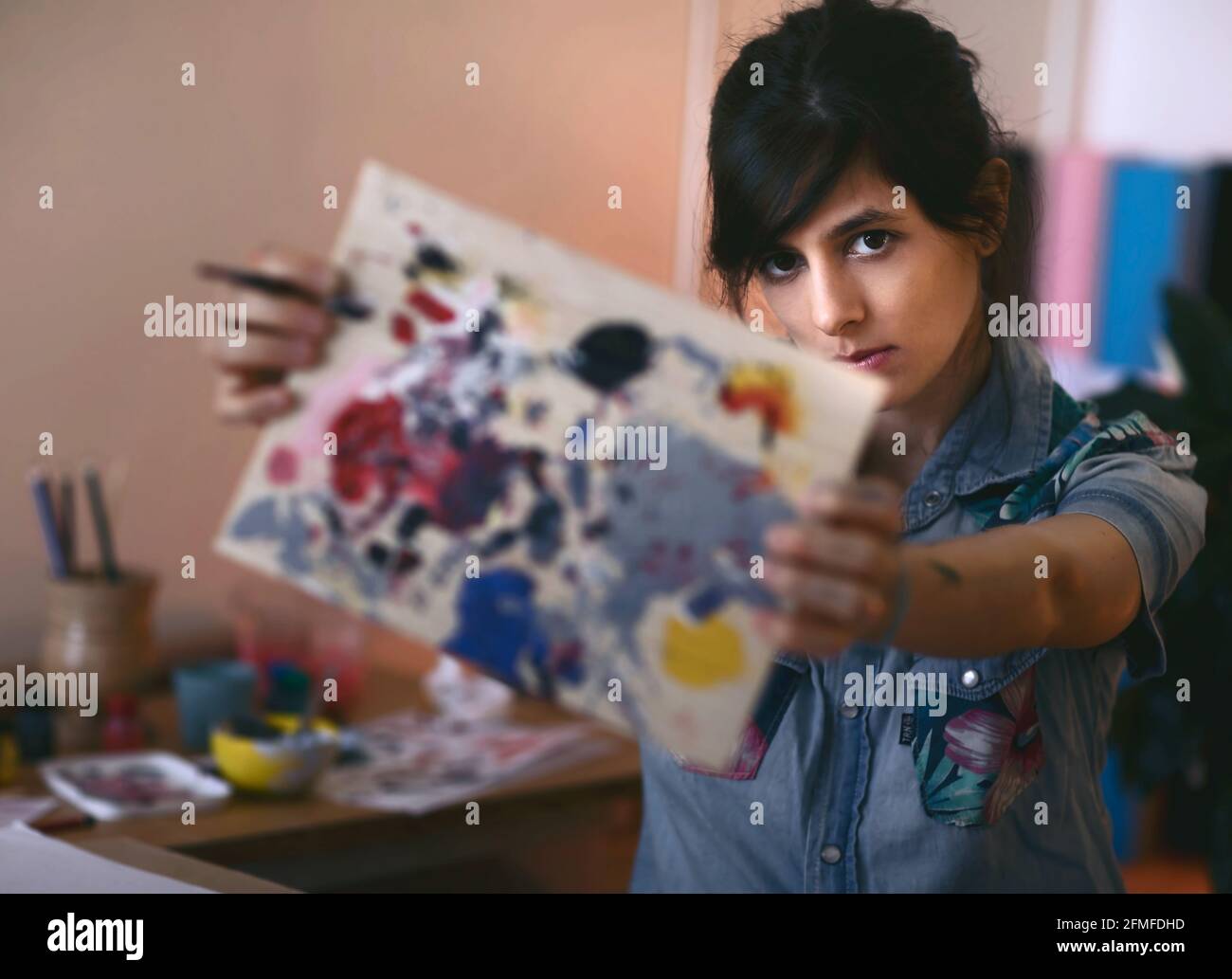Portrait of female artist with paint brush and palette in studio ...