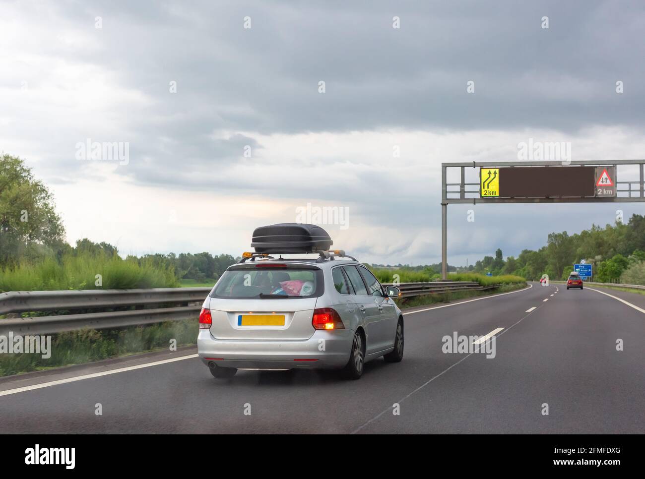 Silver car with black roof luggage box driving on the road Stock Photo