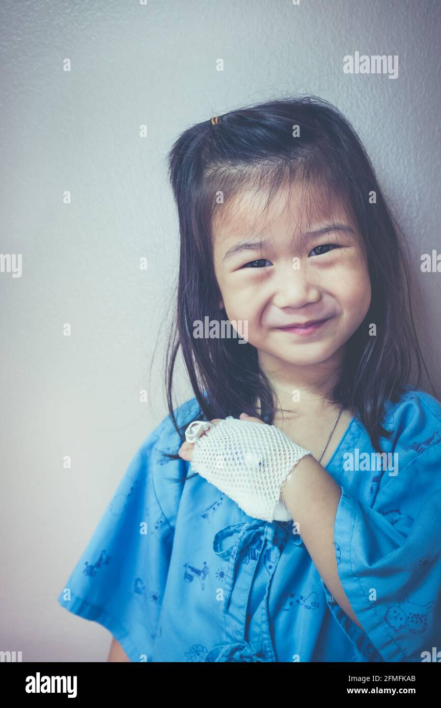 Illness asian child looking at camera, admitted in hospital and showing saline intravenous (IV) drip on her hand. Girl smiling happily. Health care st Stock Photo