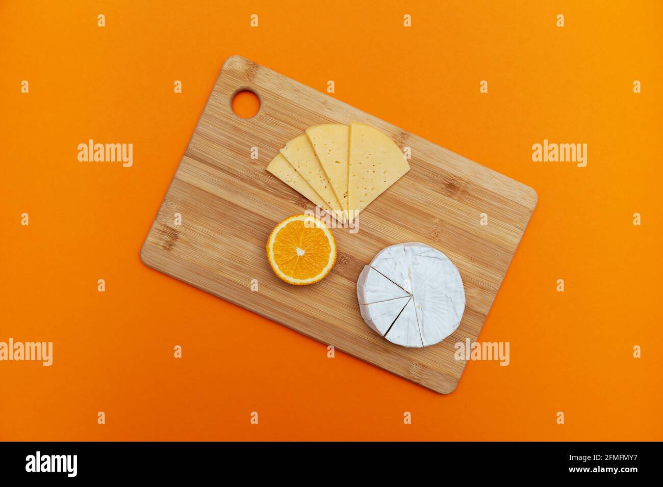 Wooden board with different cheeses and orange on a ginger background. Top view, flat layout. Stock Photo