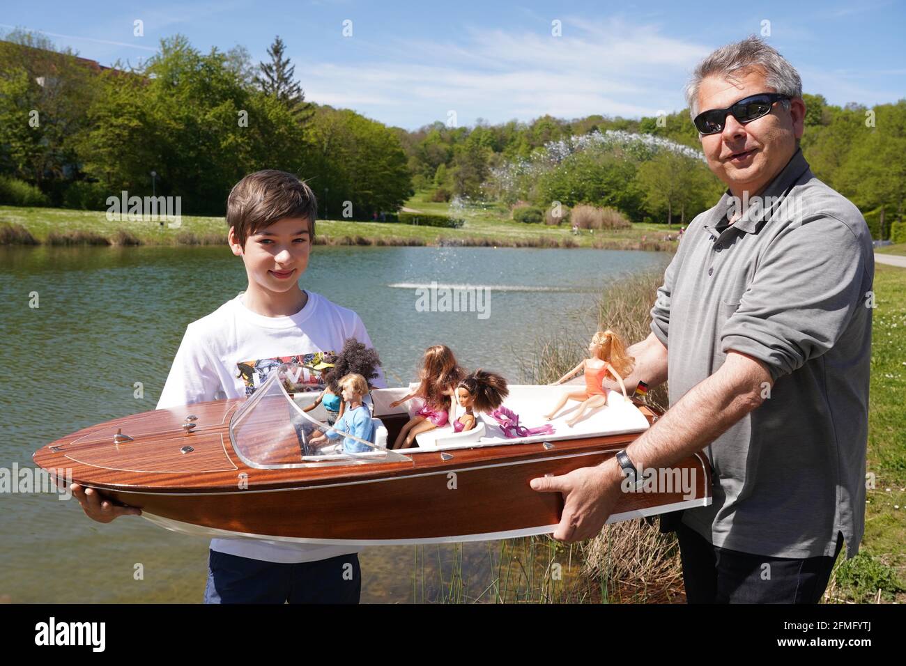 Stuttgart, Germany. 09th May, 2021. Father Steffen (56) and son Timo (11)  let their model of an e-sport boat with Barbie dolls on board sail across  the Egelsee on Sunday in temperatures