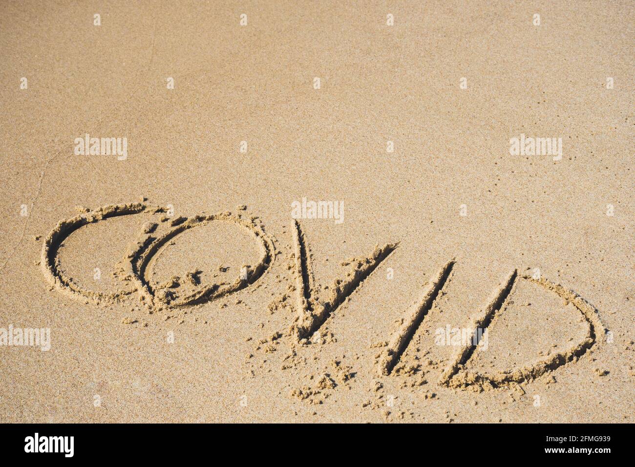 Covid written on the sand of a beach with wave washing the word, erasing or canceling it during Coronavirus summer, Covid free, safe beach, vaccine Stock Photo