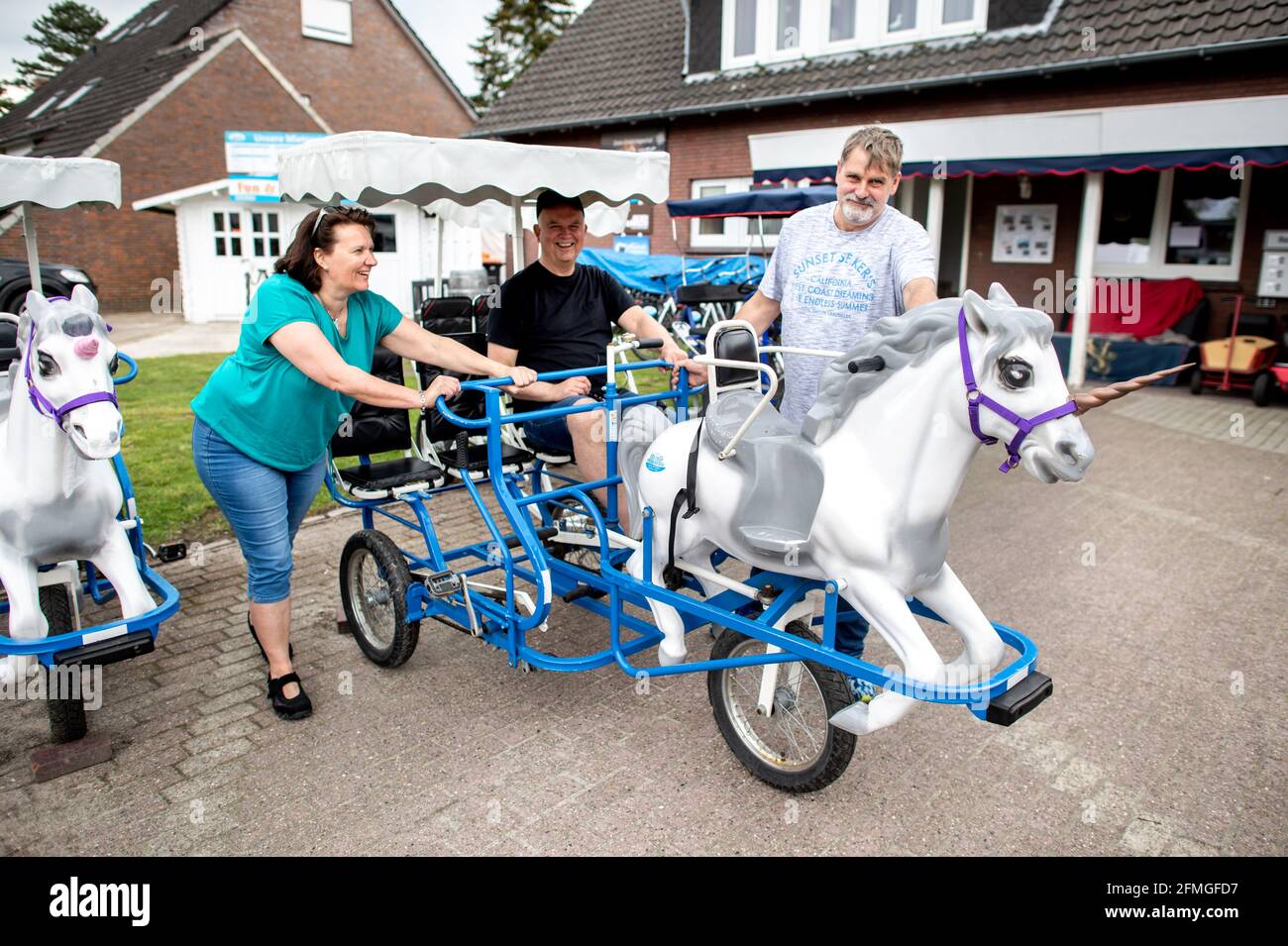 Dangast, Germany. 09th May, 2021. Peter Ihmels, an employee at a bicycle rental shop, pushes a larger family bicycle with a child's seat in the shape of a unicorn onto a parking space in almost summer-like temperatures with Claudia Kreker and Jens Redeker from Varel. Credit: Hauke-Christian Dittrich/dpa/Alamy Live News Stock Photo