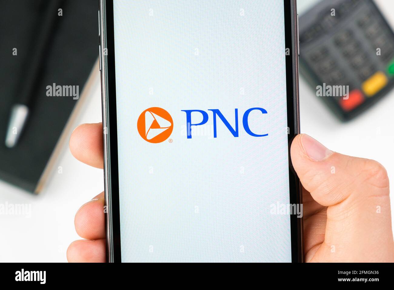 PNC bank logo on the smartphone screen in mans hand on the background of payment terminal, May 2021, San Francisco, USA Stock Photo