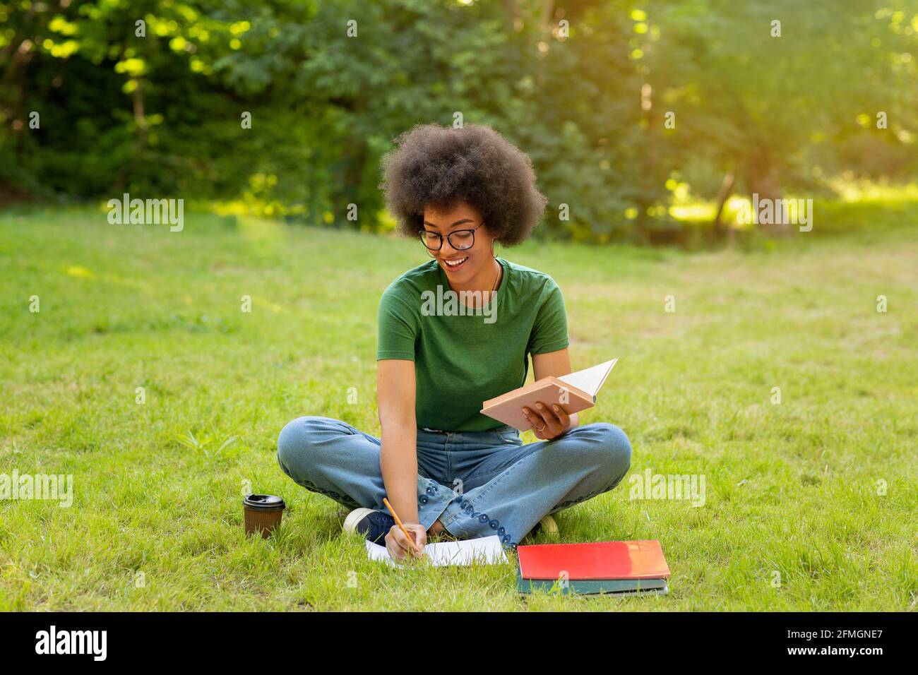 Cheerful African Student Girl Preparing Lessons Outdoors, Reading Book And Taking Notes Stock Photo