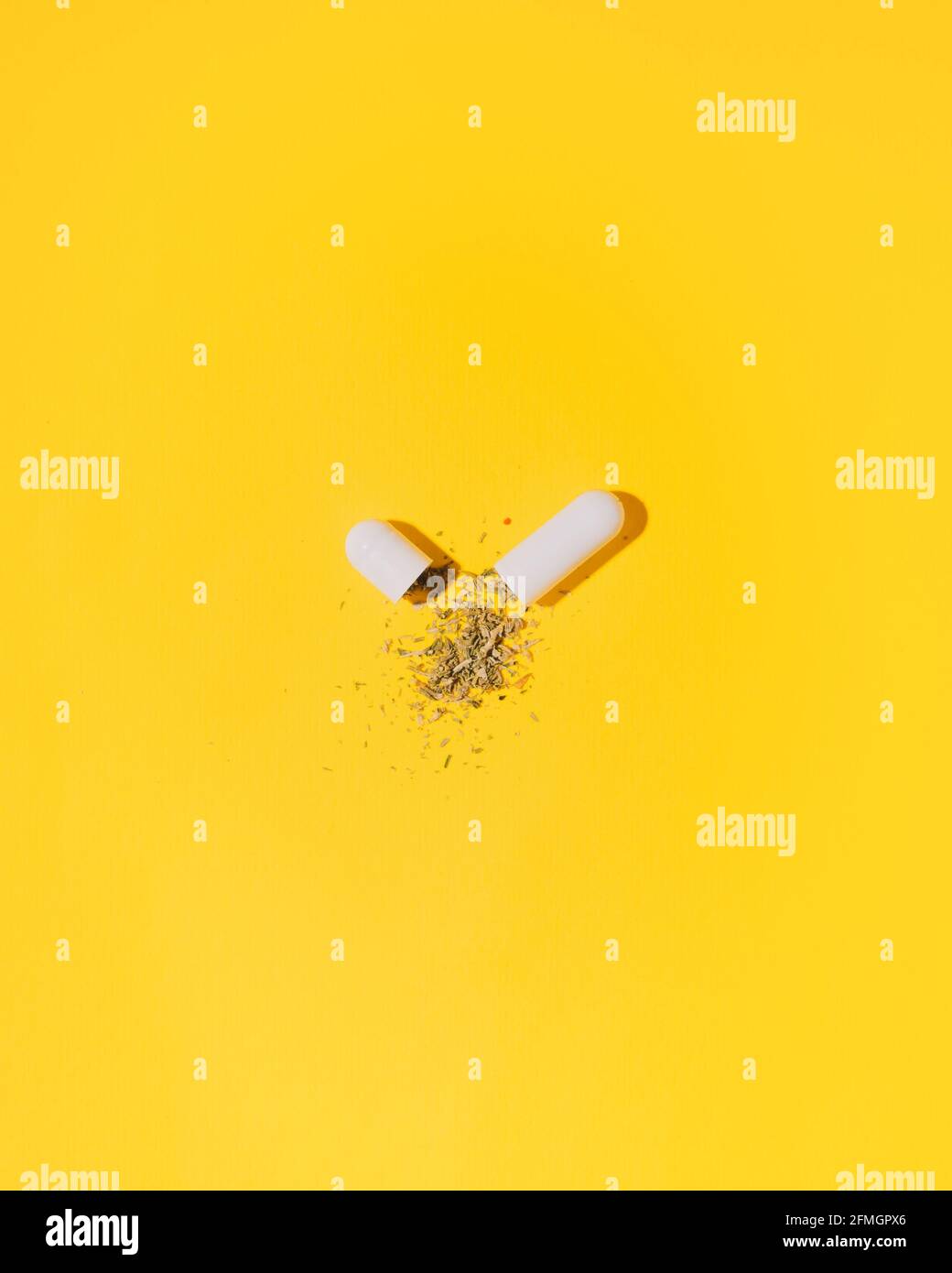 White capsule with dry herbsal or cannabis leaf inside, against bright