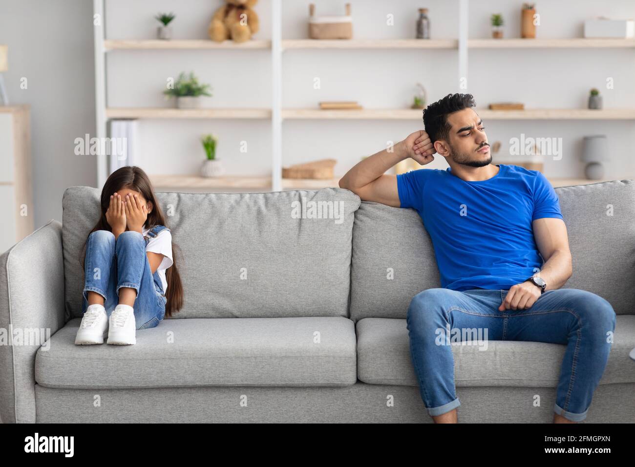 Father sitting separate on couch with offended crying little girl Stock Photo