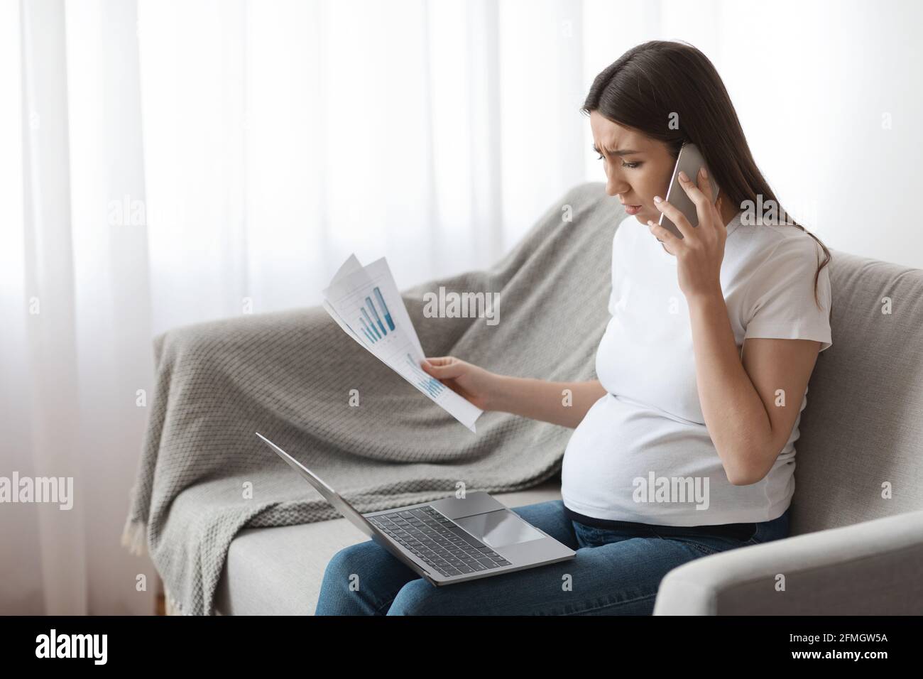 Remote Work During Pregnancy. Stressed Pregnant Woman Working With Papers And Laptop Stock Photo