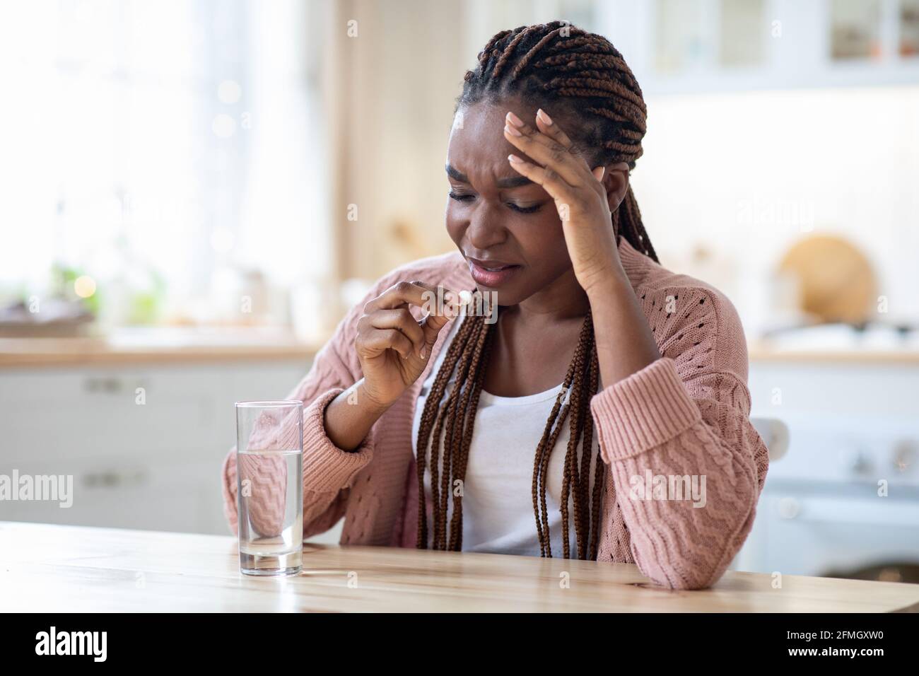 Stressed Black Lady Taking Painkiller Pill While Sitting At Table In Kitchen Stock Photo