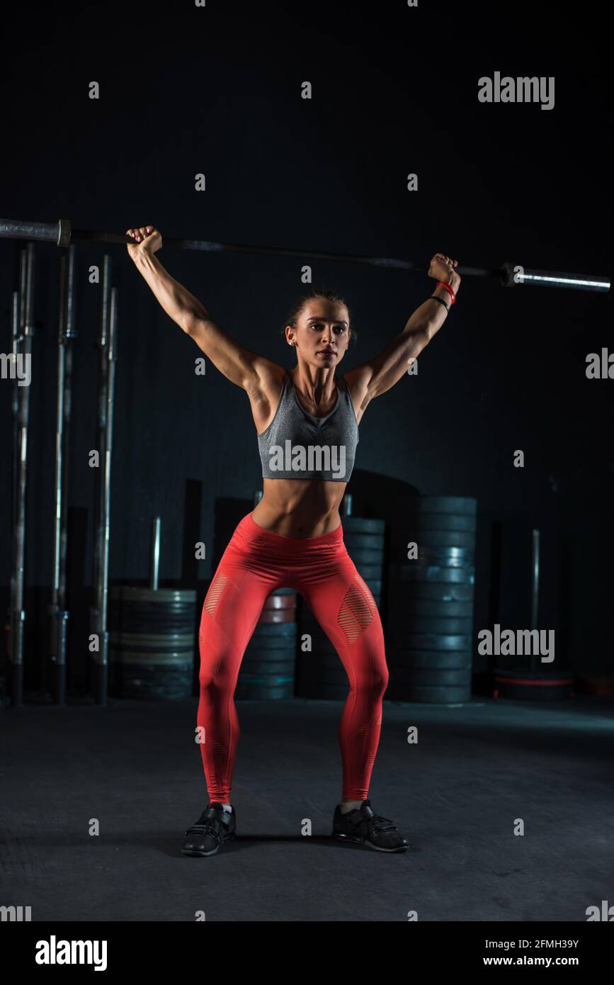 Young, European, muscular girl in red leggings, doing exercise with a  barbell in the gym for crossfit. Dark background Stock Photo - Alamy