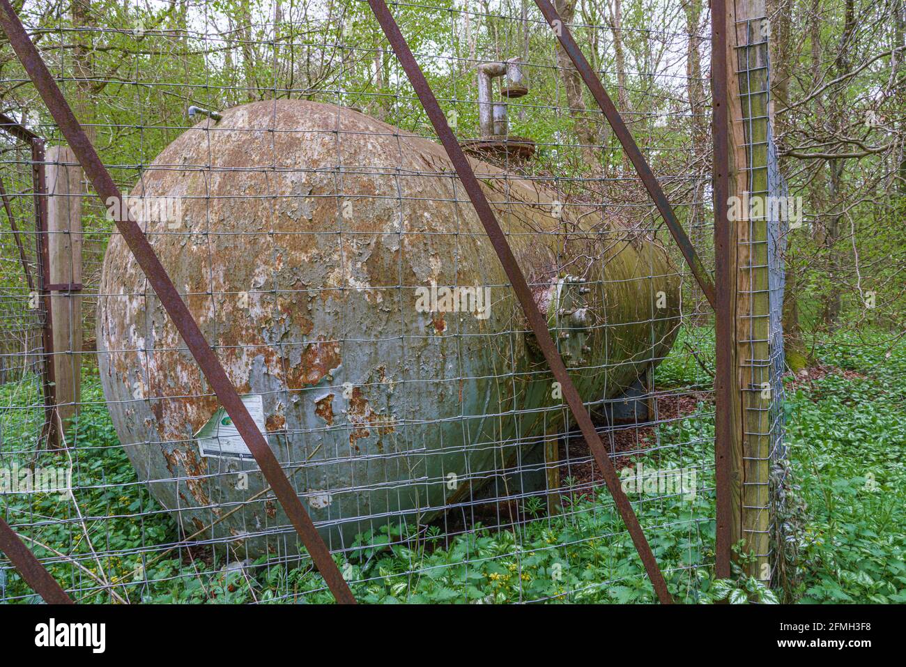 a large metal storage tank rusting away in a dense woodland location Stock Photo