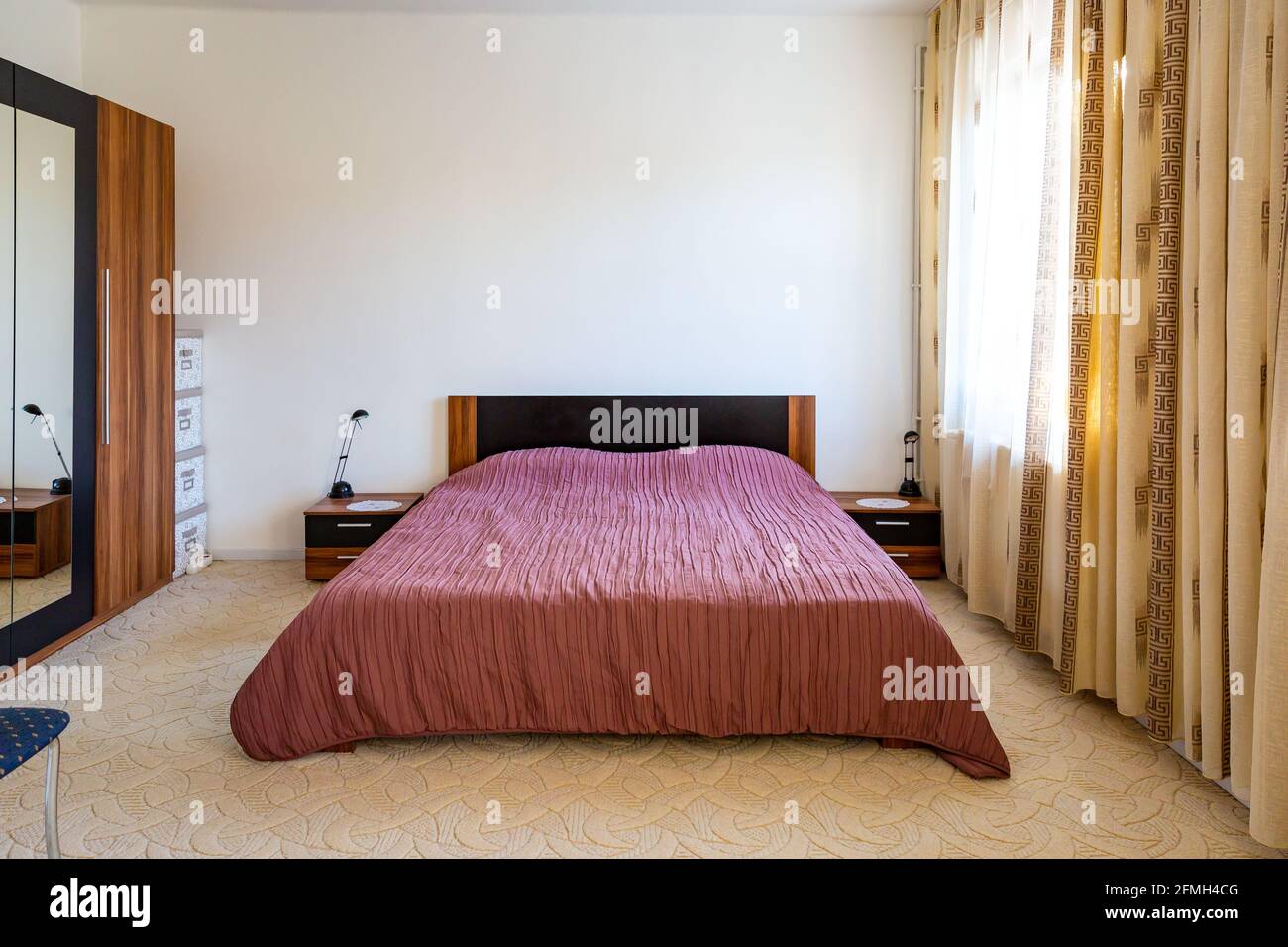 Cozy bedroom interior with wide double bed covered with pink bedspread. Stock Photo