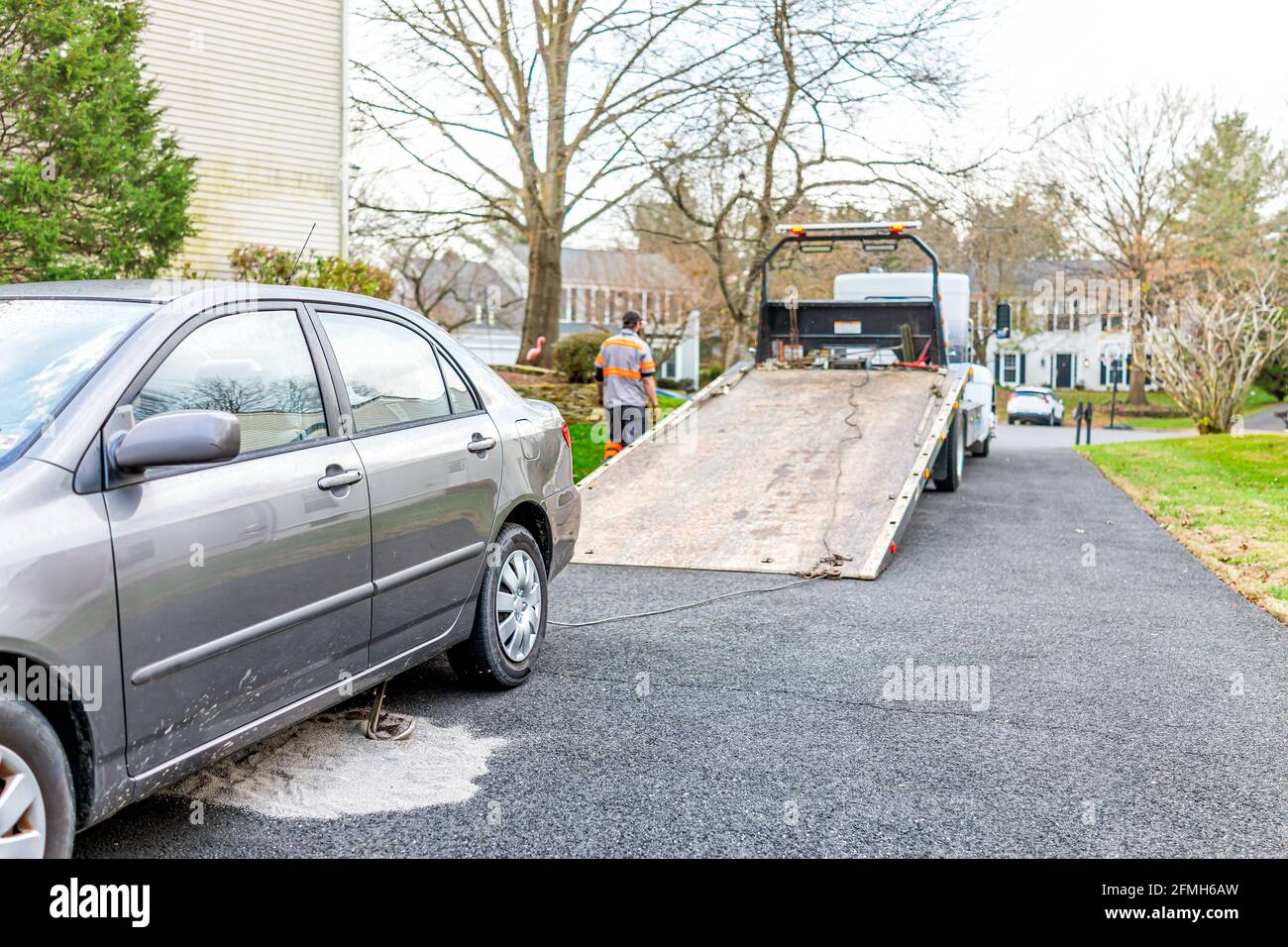 Car in driveway with tower man working to tow vehicle due to fuel leak