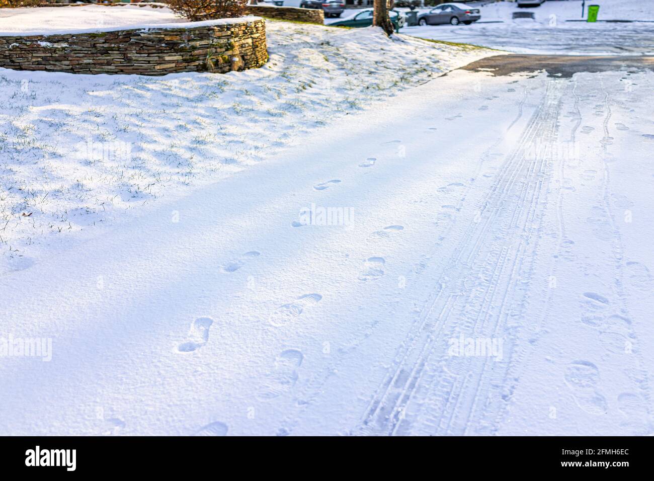 Blue driveway of house in neighborhood with snow covered ground from white storm in Virginia suburbs with footprints and car tracks on road street shi Stock Photo