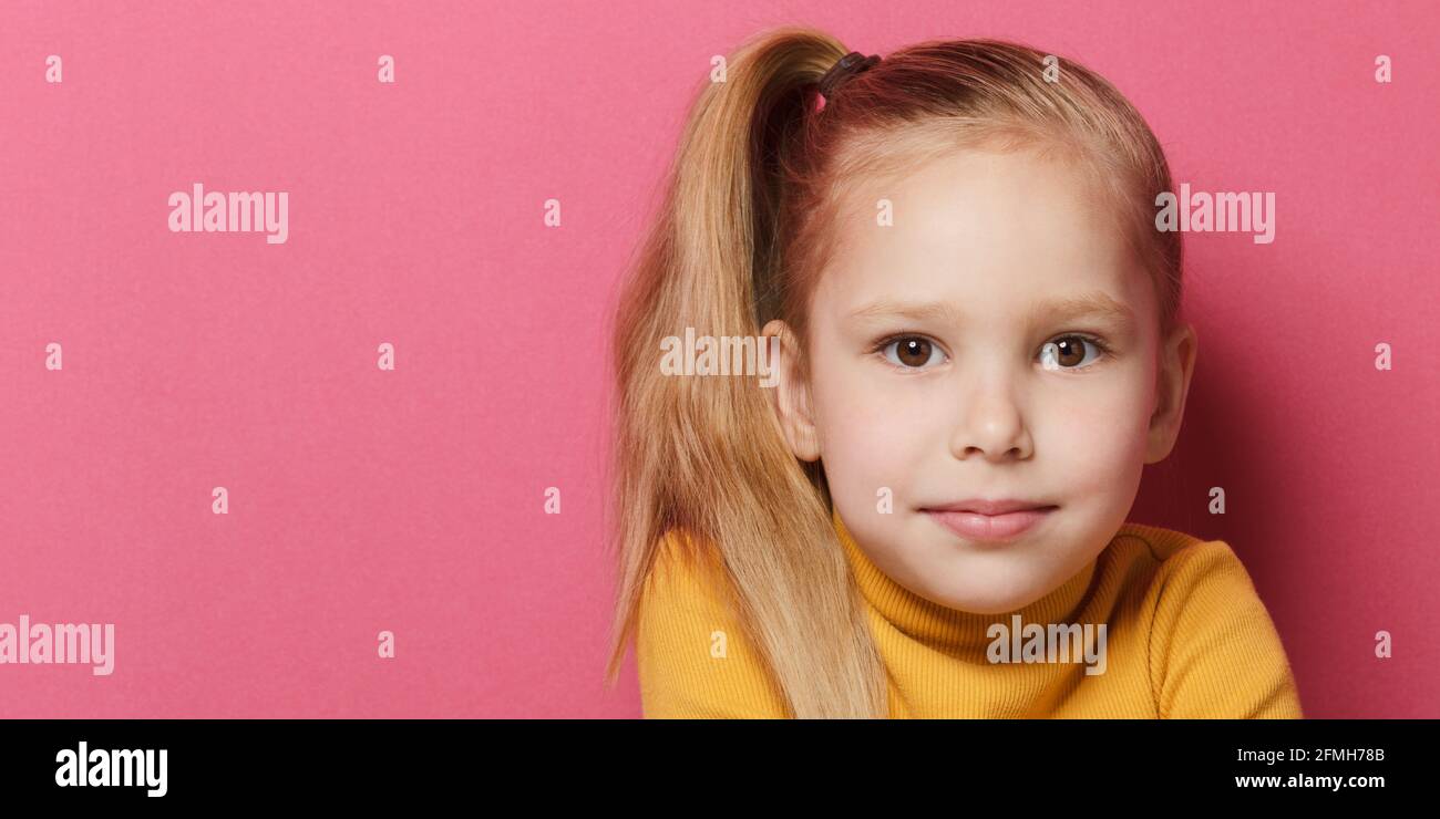Close up portrait of cute girl 5 year old posing in studio wearing yellow turtleneck over pink background. Stock Photo