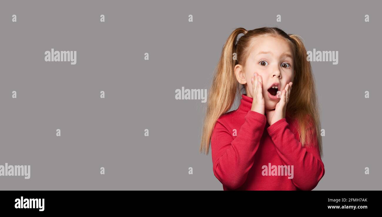 Surprised child girl holding her cheeks with her hands opening her ...