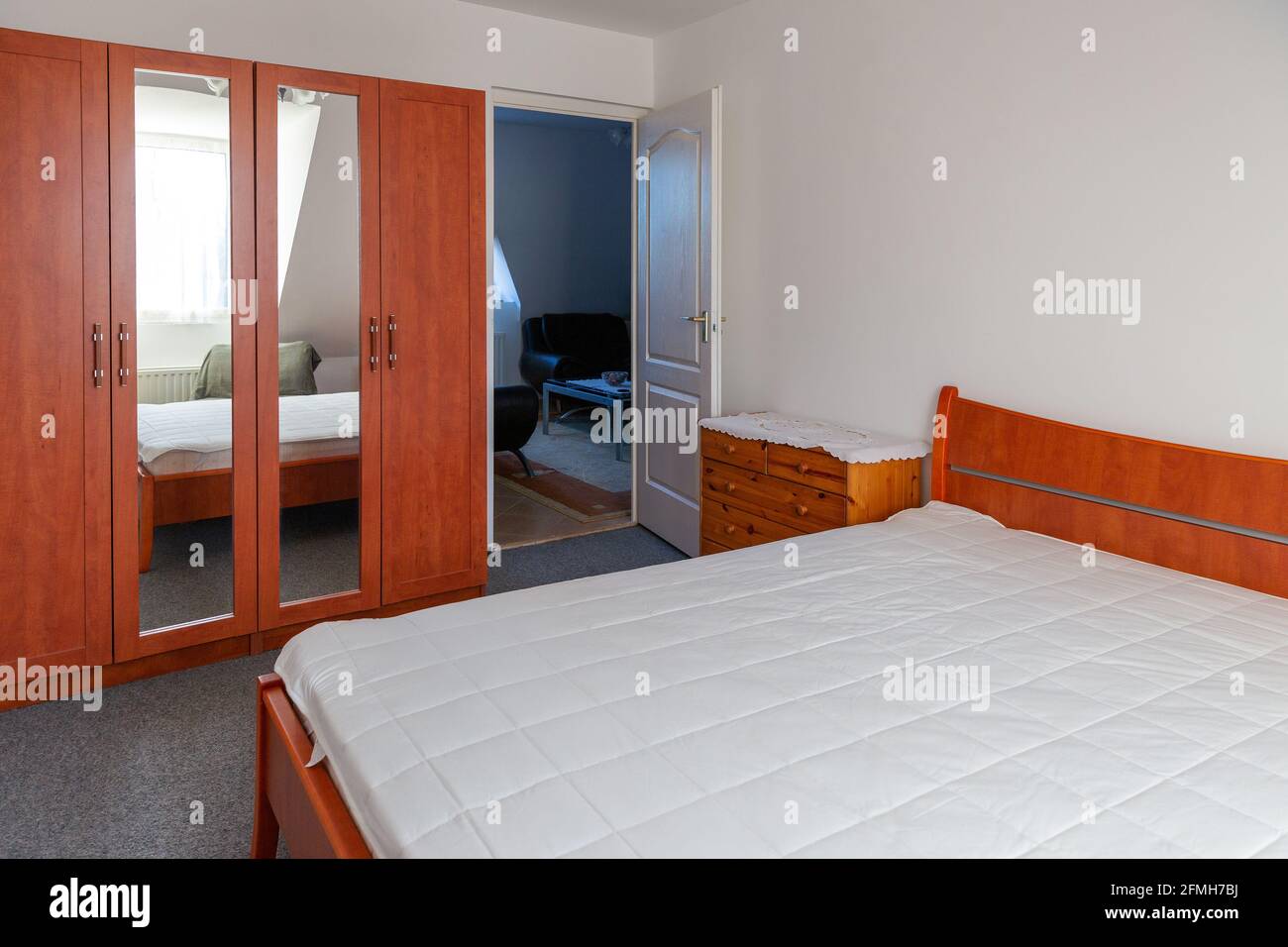 Cozy bedroom interior with wide double bed covered with white mattress protector. Stock Photo