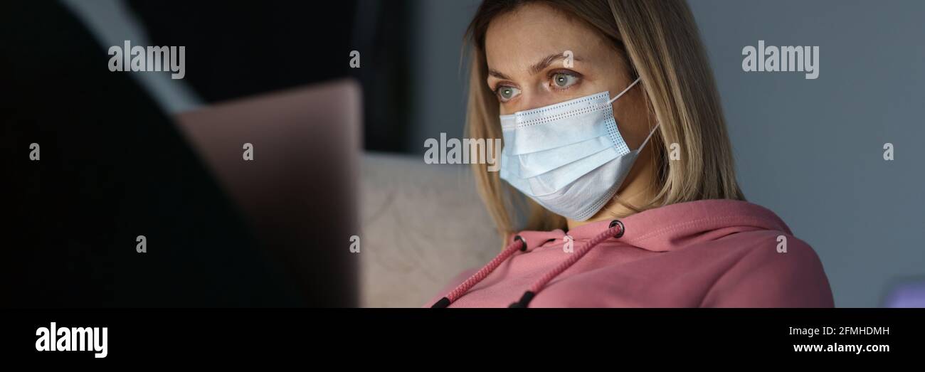 Young woman in protective medical mask sitting in front of laptop at home Stock Photo