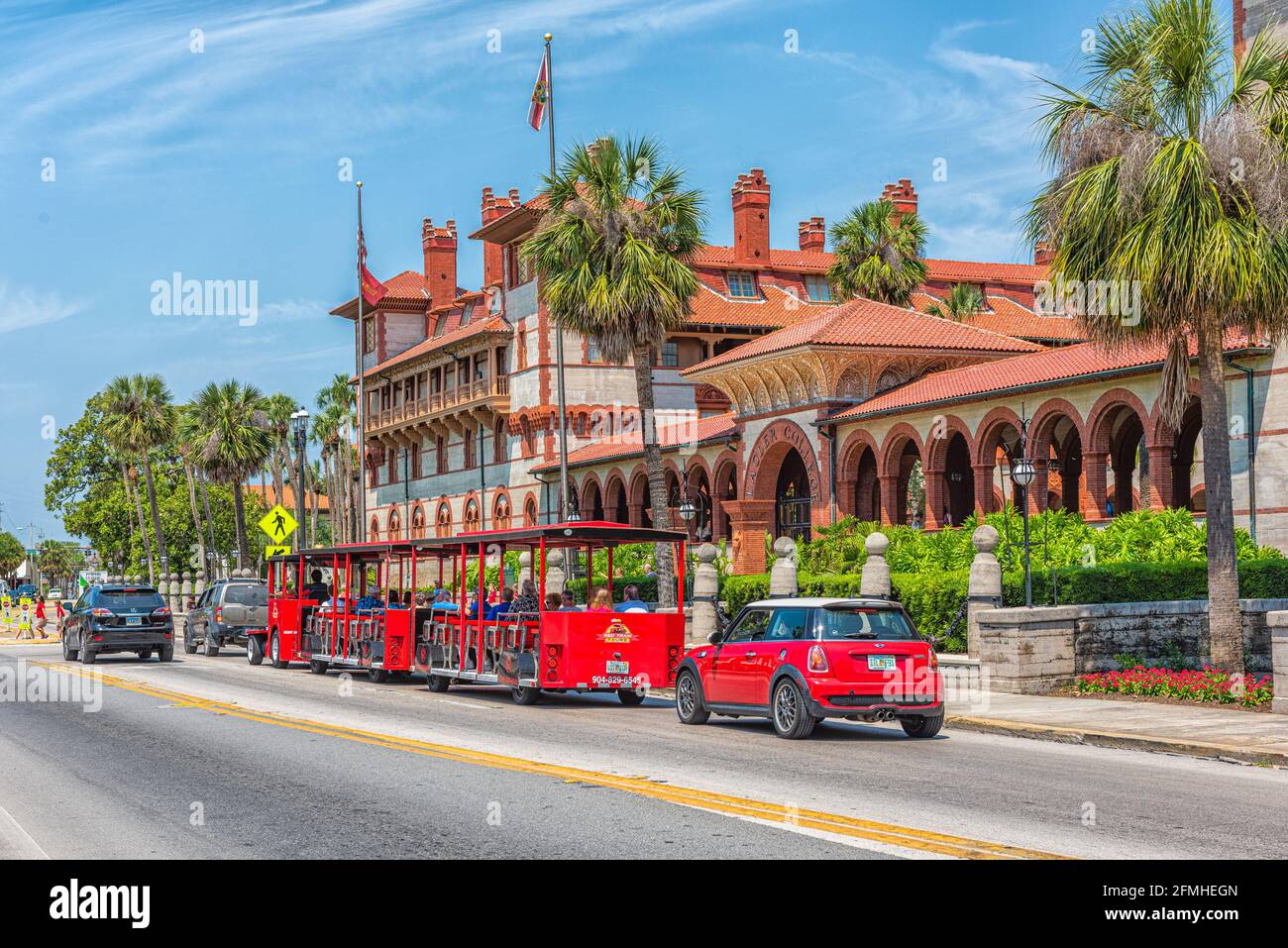 St. Augustine, USA - May 10, 2018: Flagler College with Florida architecture in historic city and red train trolley tour guide tram riding on street r Stock Photo