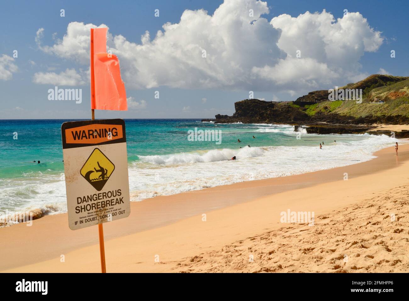 "Warning Dangerous Shorebreak" sign posted and flagged at Makapuu Beach with volcanic rocks in