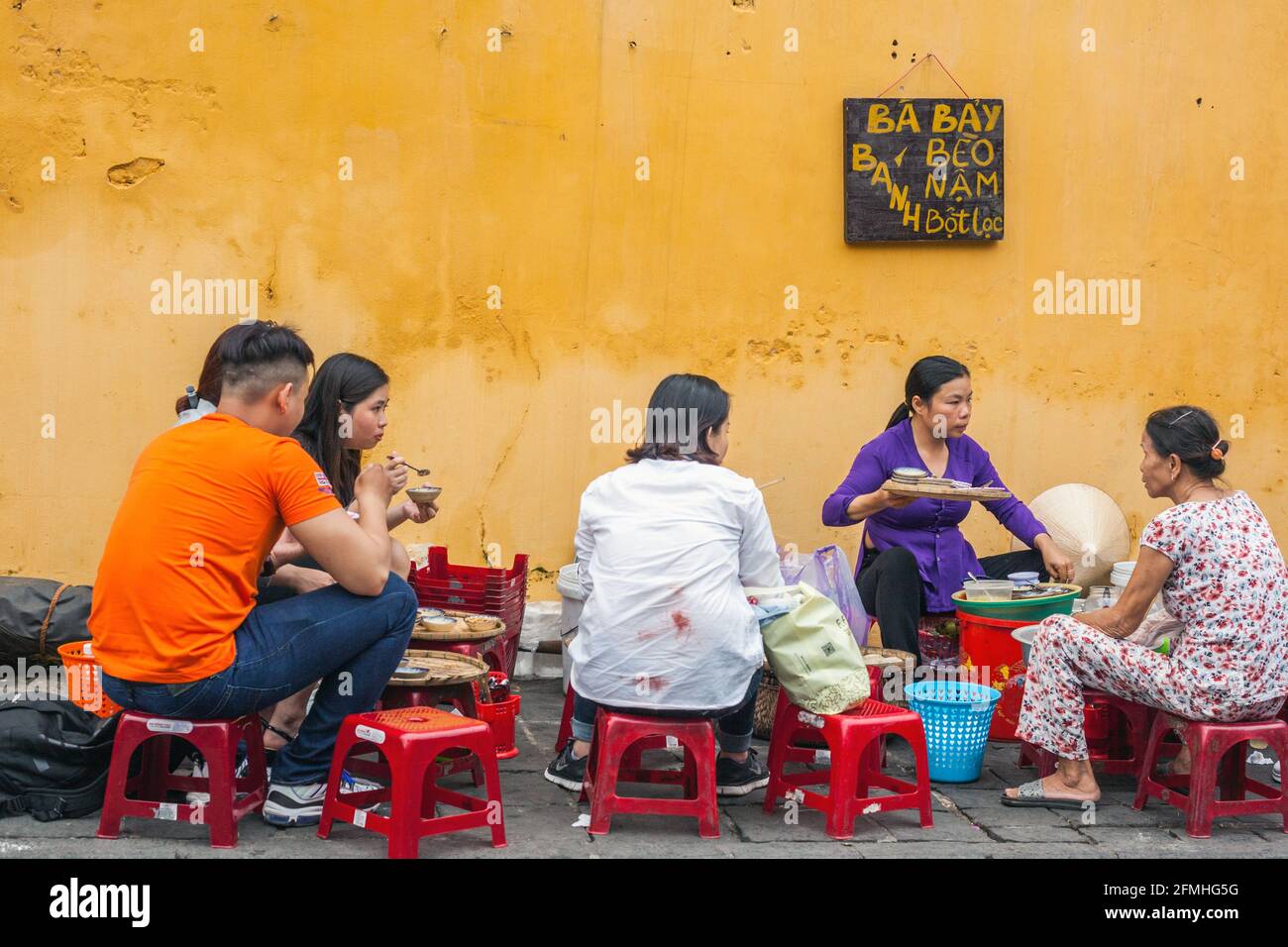 Vietnamese females sat on tiny stools eating street food from roadside