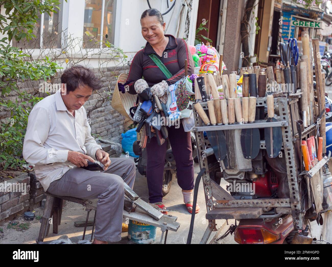Vietnamese handyman with motorbike full of tools and equipment sits roadside working, Hoi An, Vietnam Stock Photo