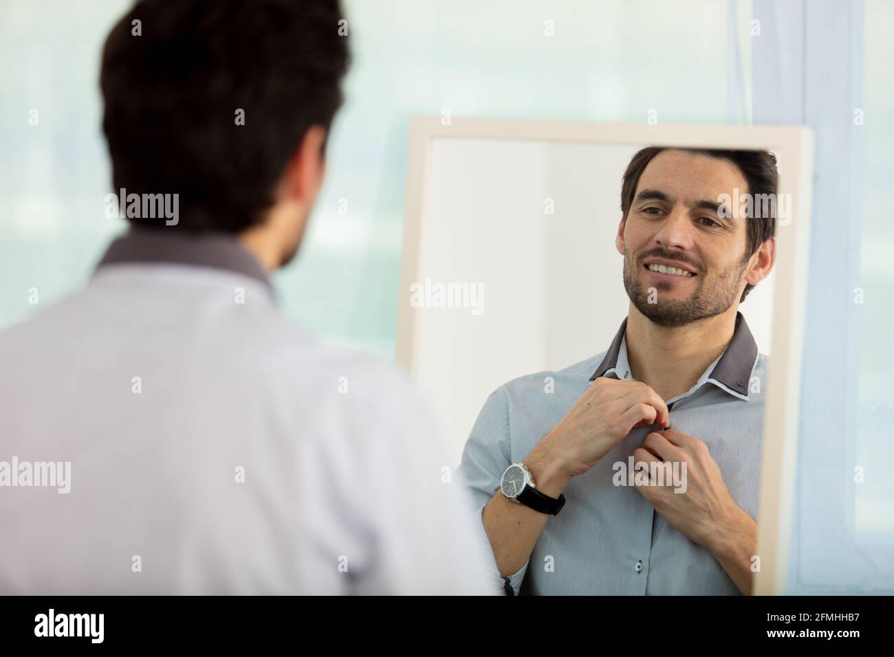 man getting dressed in bedroom while looking at mirror Stock Photo
