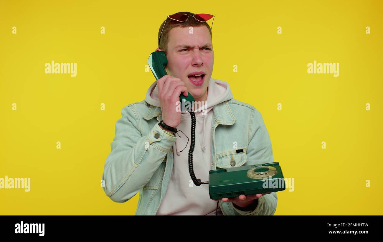 Crazy sincere teen man talking on wired vintage telephone of 80s, fooling, making silly funny faces Stock Photo