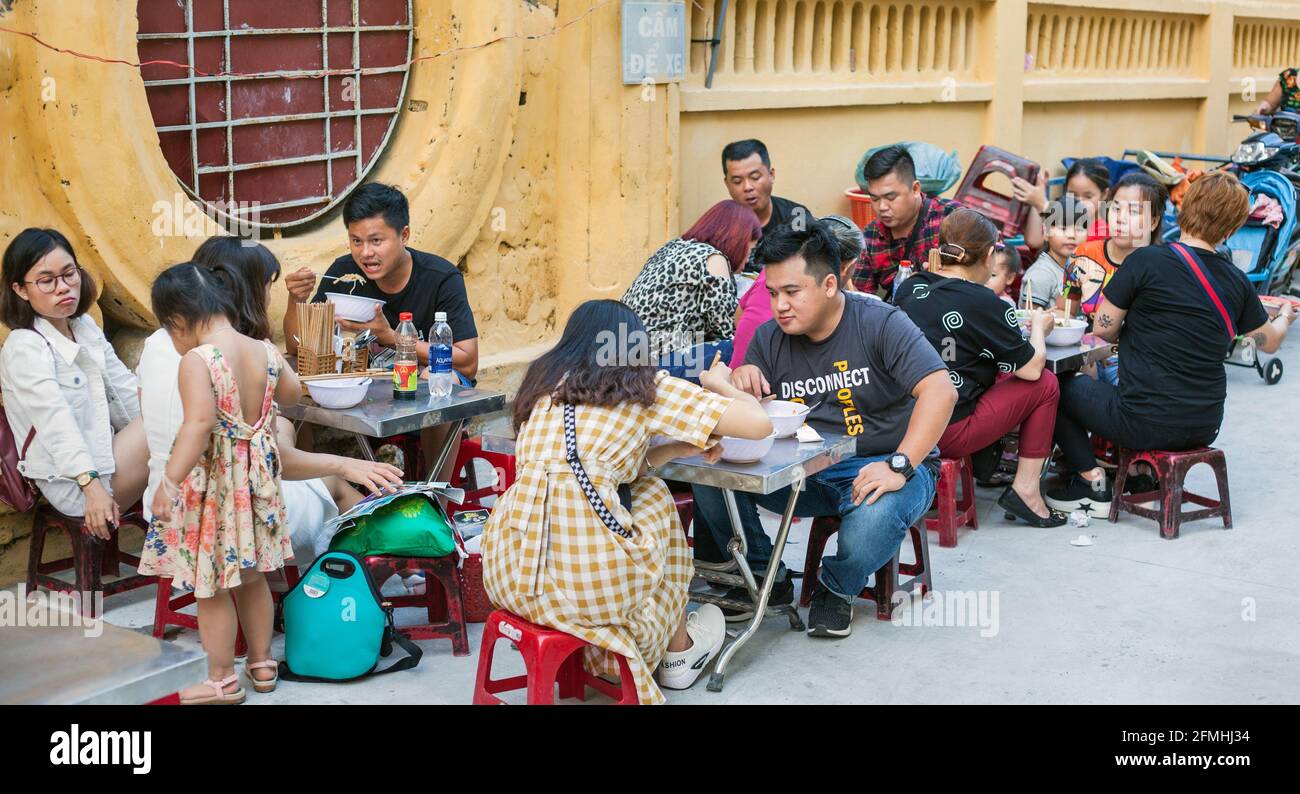 Vietnamese families eating street food at pavement cafe, Hoi An