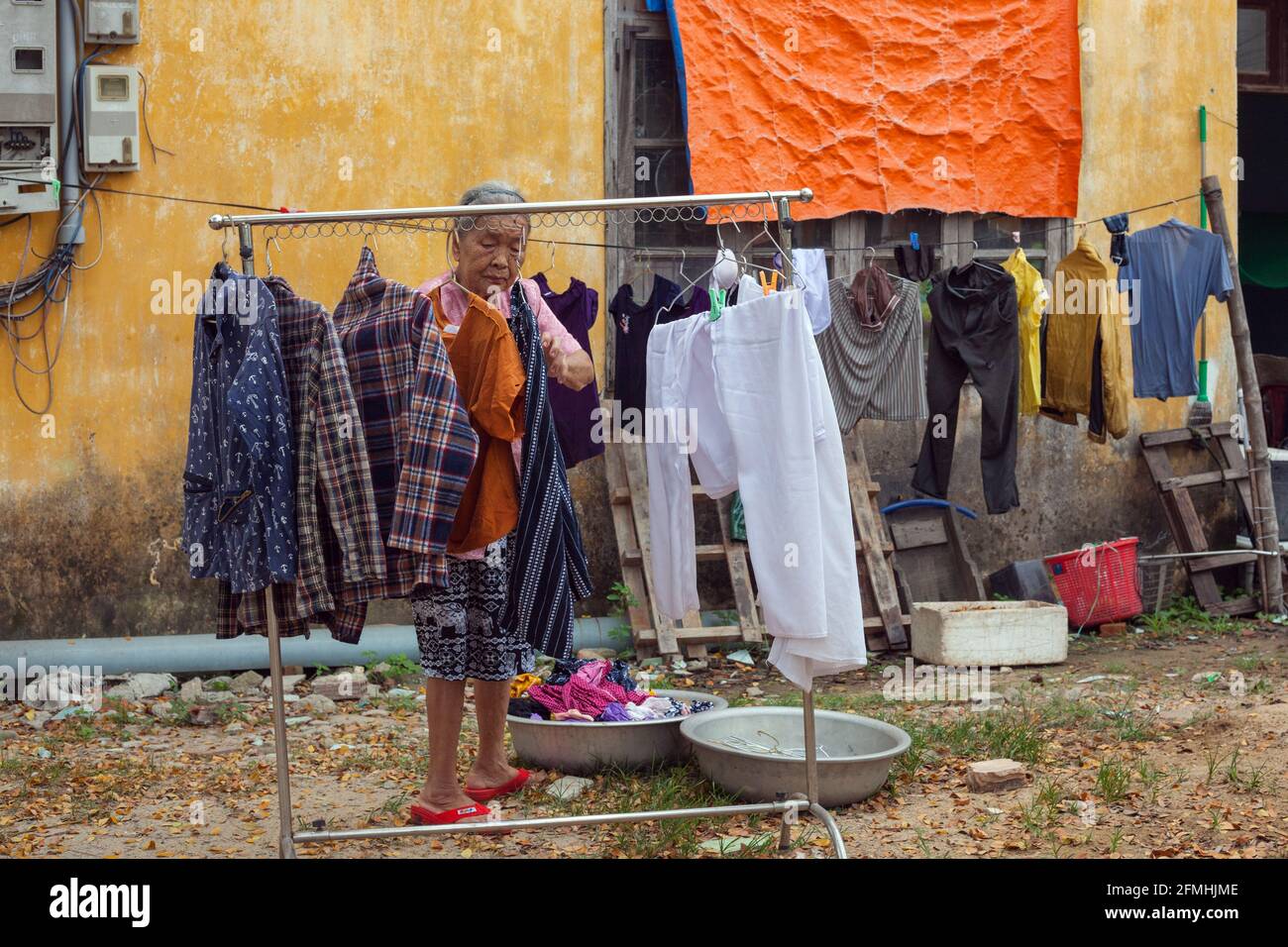 Elderly Vietnamese lady hanging clothing on washing line outside house in Hoi An, Vietnam Stock Photo