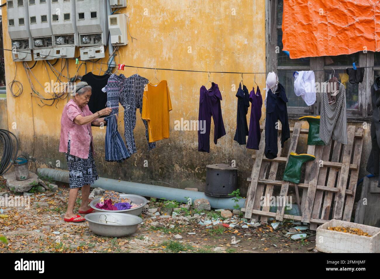 Elderly Vietnamese lady hanging clothes on washing line outside home in Hoi An, Vietnam Stock Photo