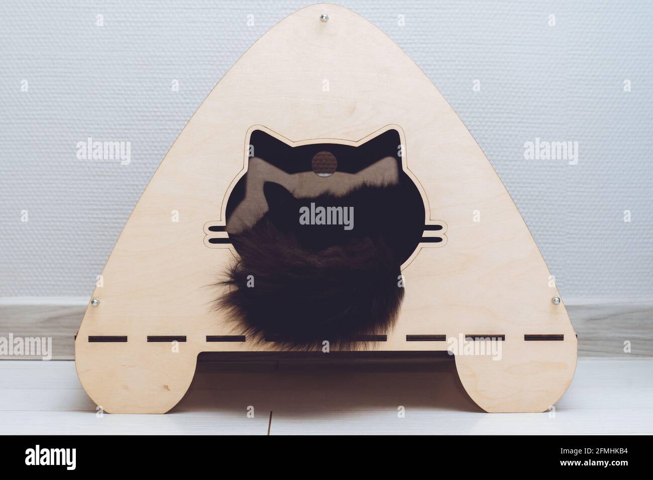 Wooden cat house made of plywood with entrance in form of cat's face, with black cat's tail, sticking out of it Stock Photo