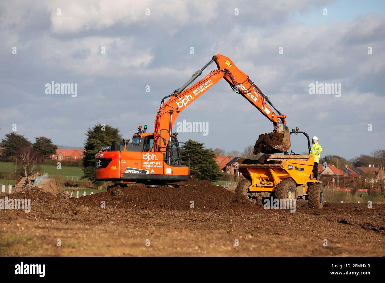 A digger and a truck pictured preparing land on the early stages of a Linden Homes housing development in Chichester, West Sussex, UK. Stock Photo