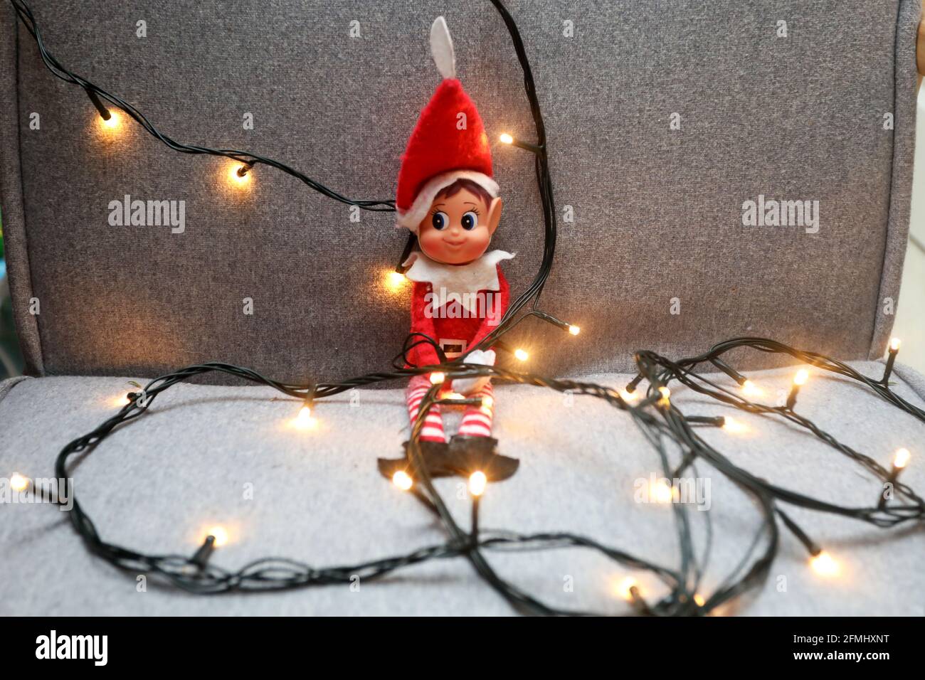 An Elf on the shelf pictured wrapped up in Christmas lights on a chair in West Sussex, UK. Stock Photo