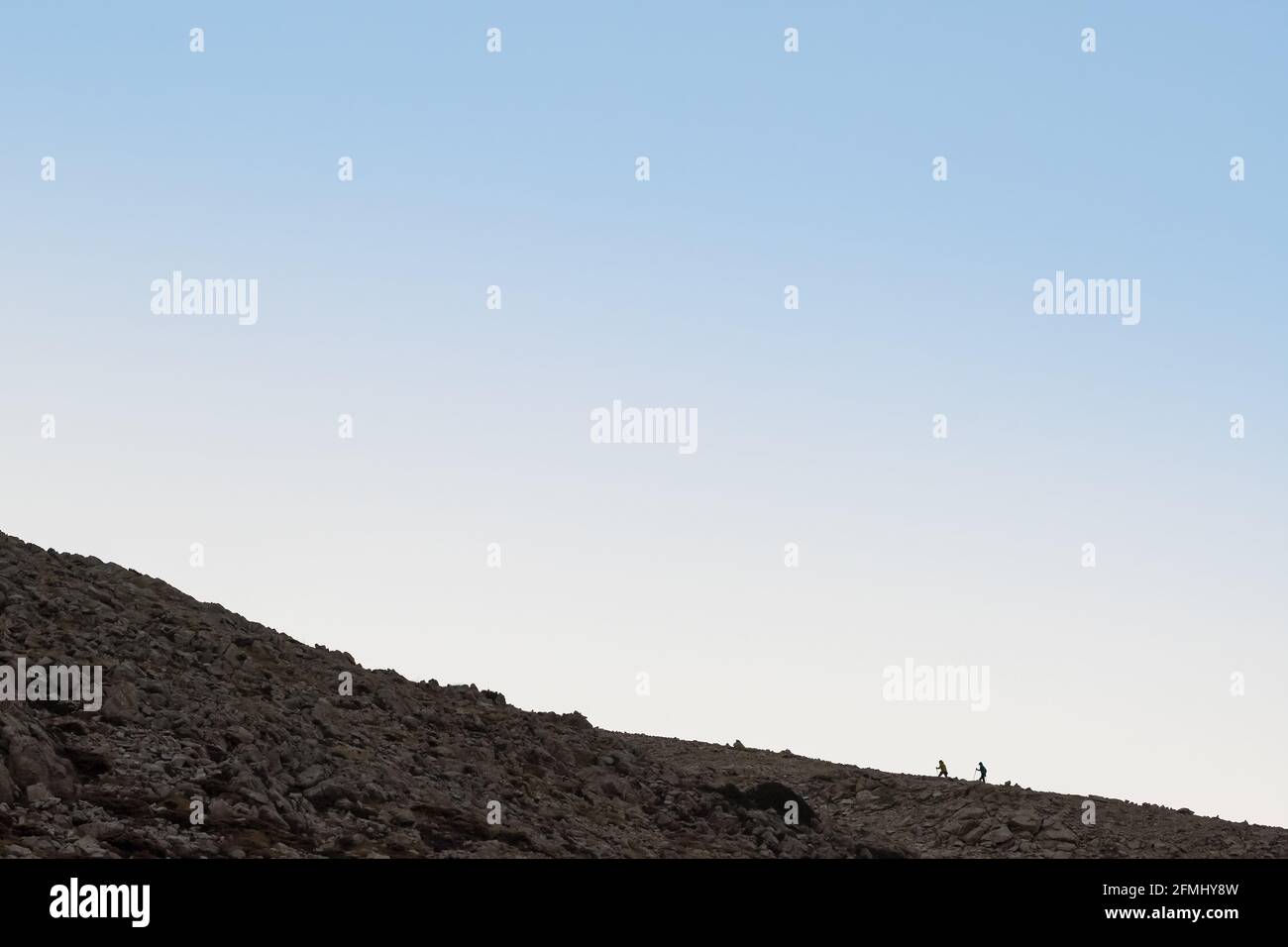 Silhouette of two tourists with trekking poles climbing mountain at sunrise Stock Photo