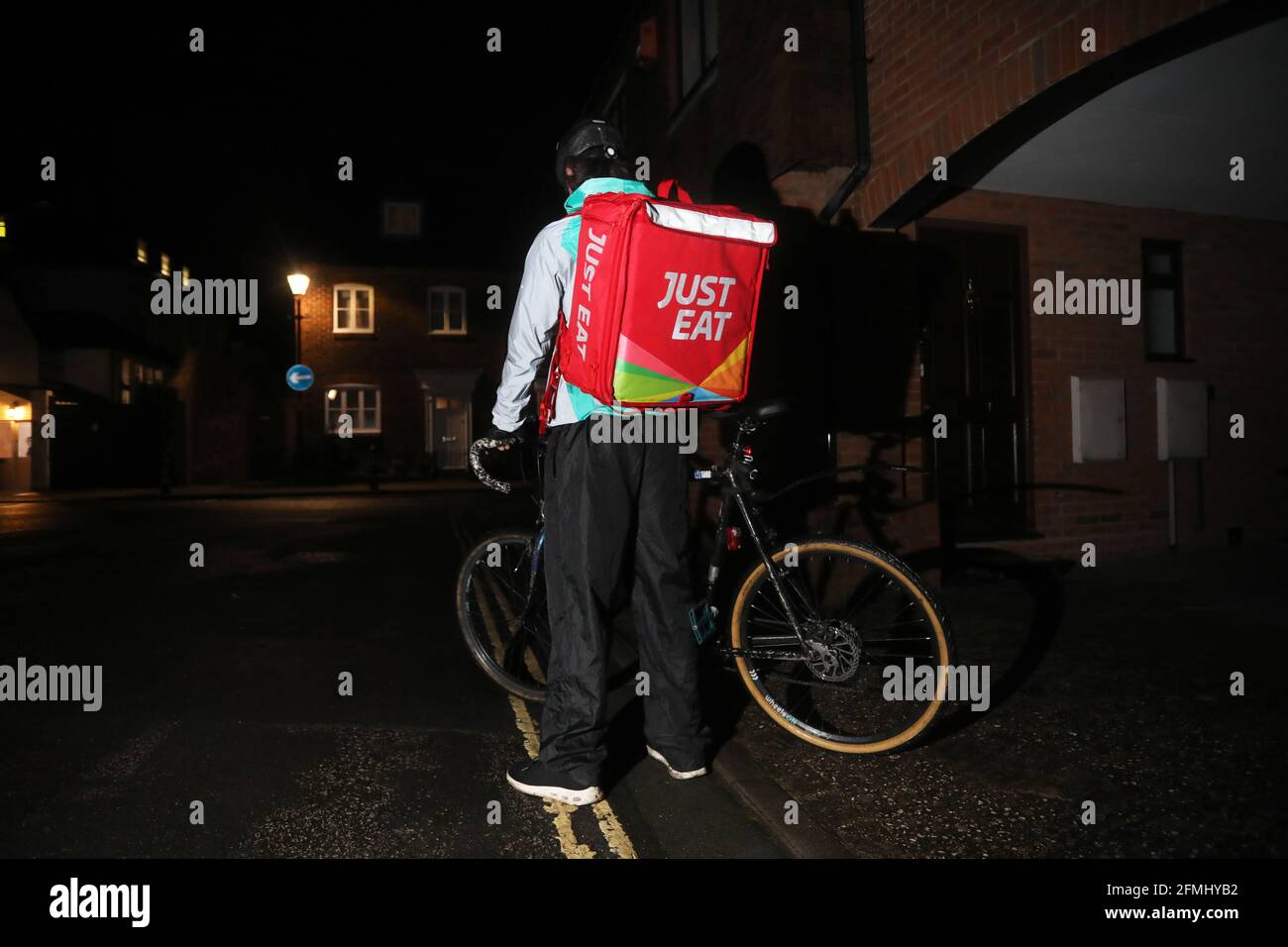 A Just Eat delivery man on his bike in the dark streets of Chichester, West Sussex, UK. Stock Photo