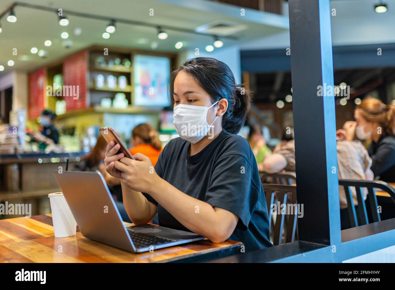 Woman wearing mask and using smartphone in cafe Stock Photo