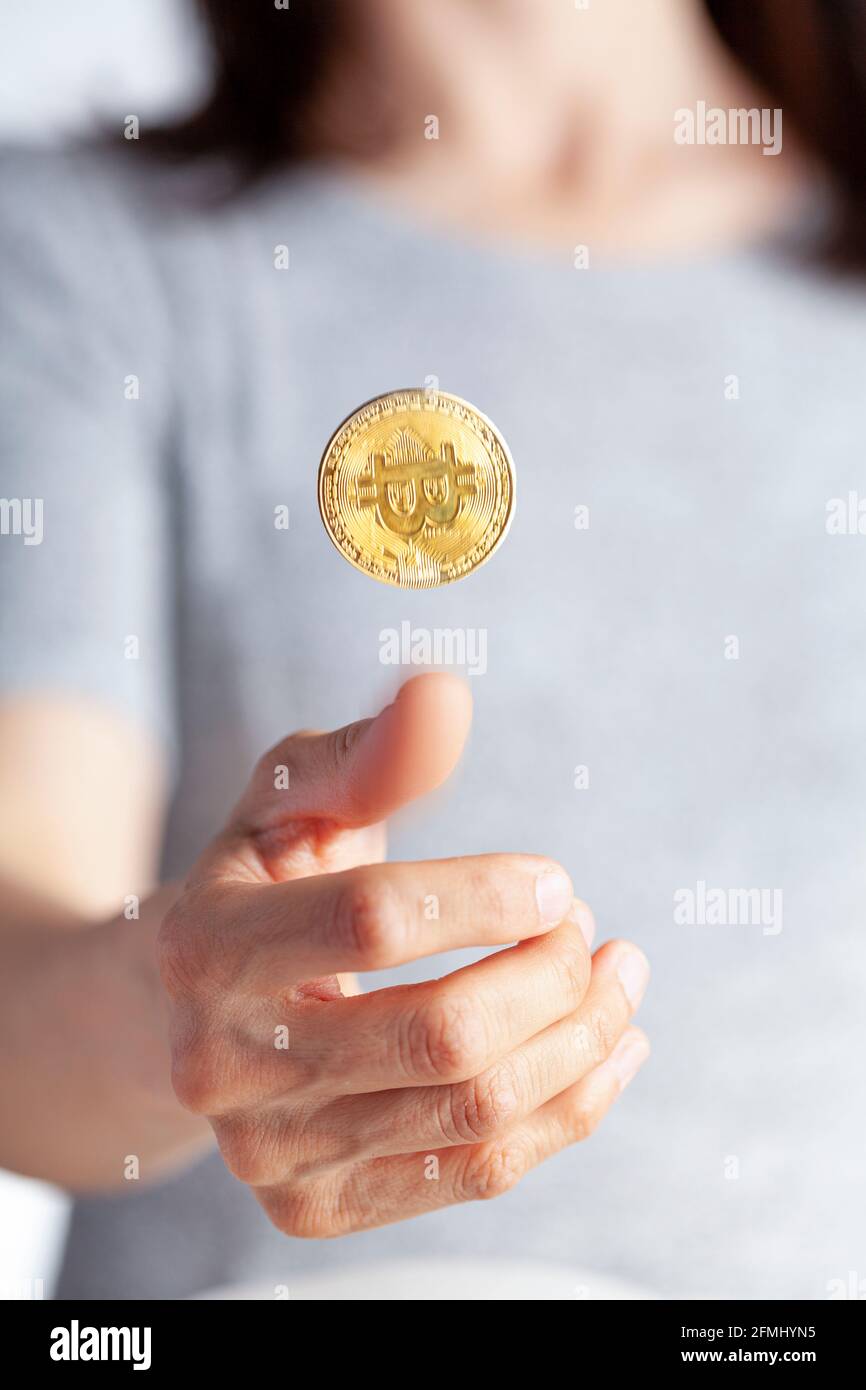 a woman is flipping a coin using a bright colored bitcoin. A concept image for investing in crypto currency and its risky uncertain nature. It can go Stock Photo