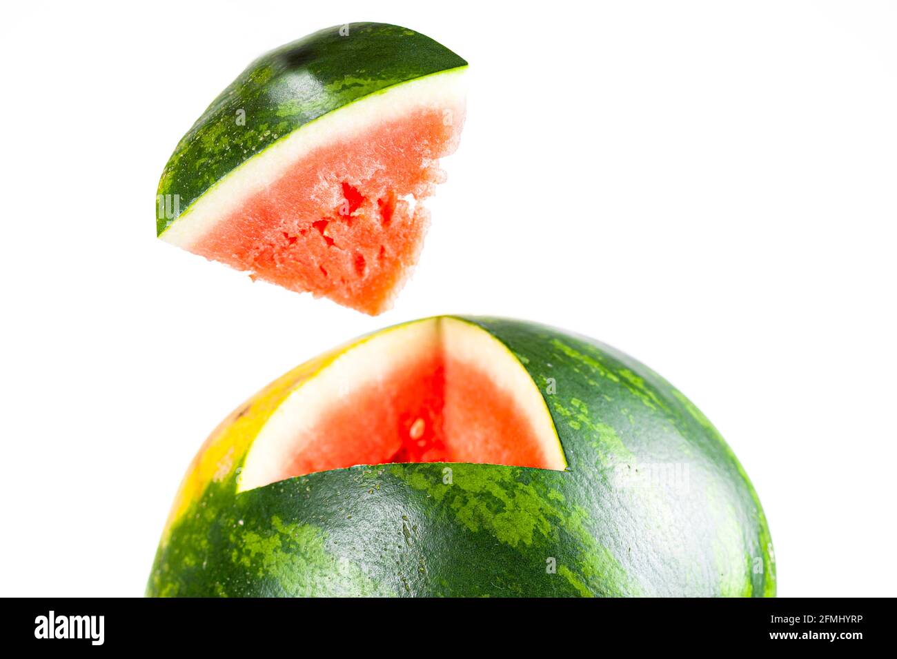 A green ripe watermelon is cut with a knife and a pyramidal wedge was carved out. Closeup image shows the wedge in air with the fitting part of the sp Stock Photo