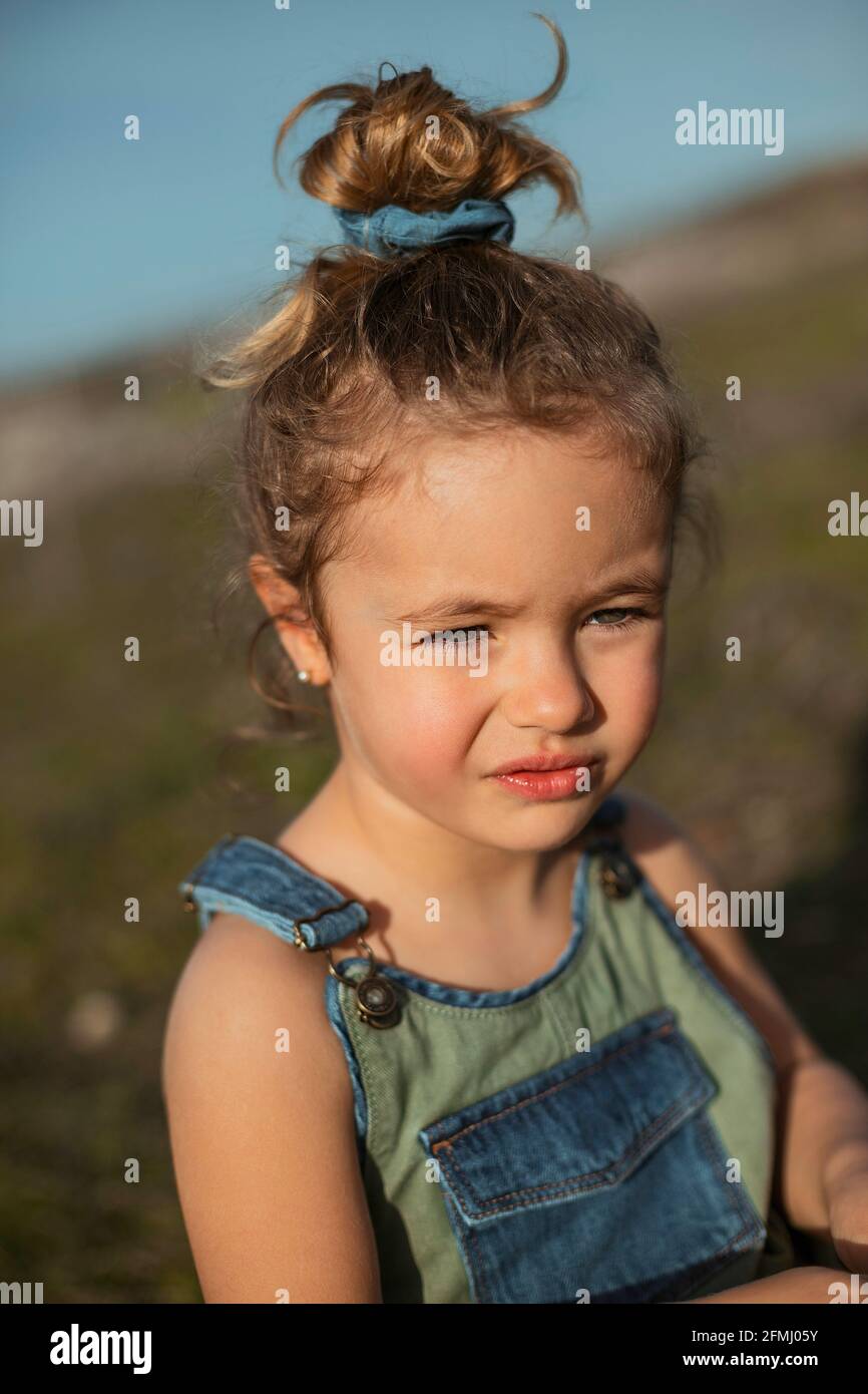 Delighted adorable little girl in overalls standing in meadow and
