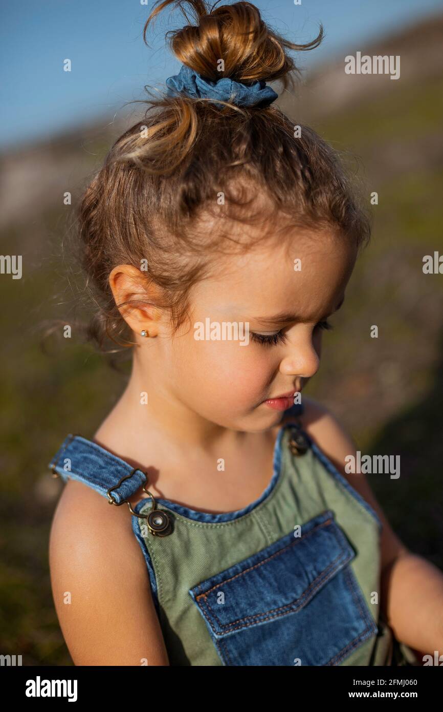 Delighted adorable little girl in overalls standing in meadow and