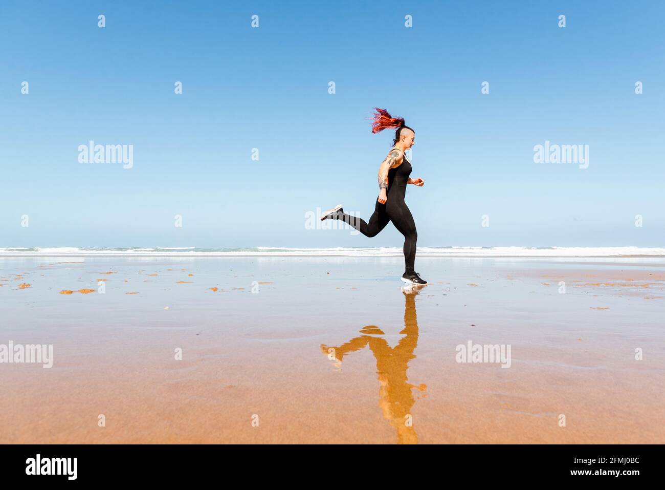 Side view of active female jogger with tattoos running on ocean shore ...