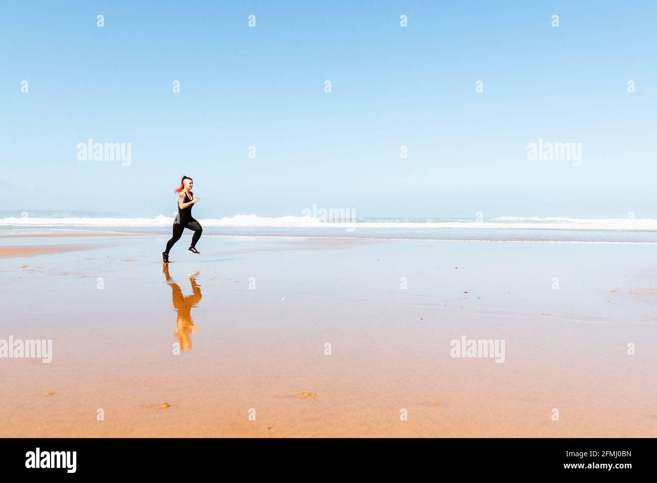 Side view of active female jogger with tattoos running on ocean shore ...