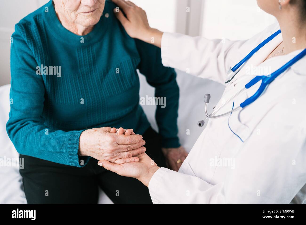 Crop anonymous doctor speaking with elderly Woman while holding hands during examination in hospital Stock Photo