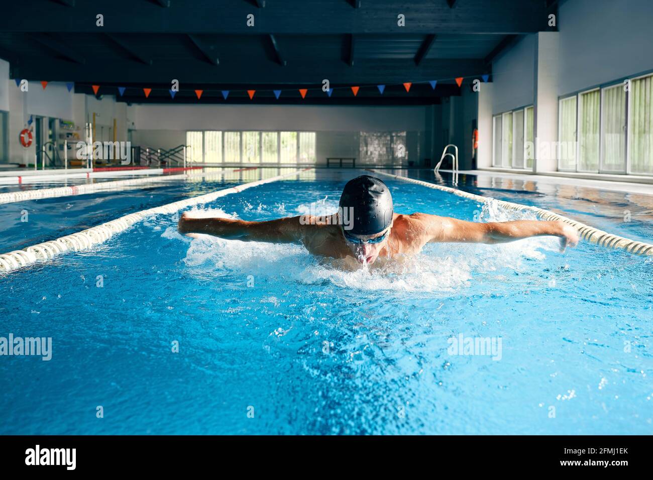 Strong male swimmer in bathing cap performing butterfly stroke during workout in swimming pool with blue water Stock Photo