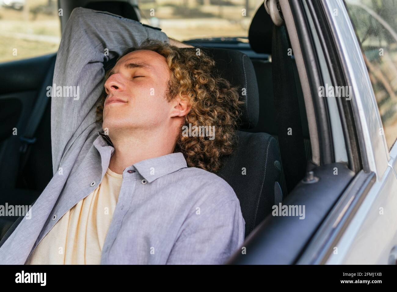 Relaxed young male traveler sleeping on driver seat of modern automobile while resting during road trip through countryside in summer day Stock Photo