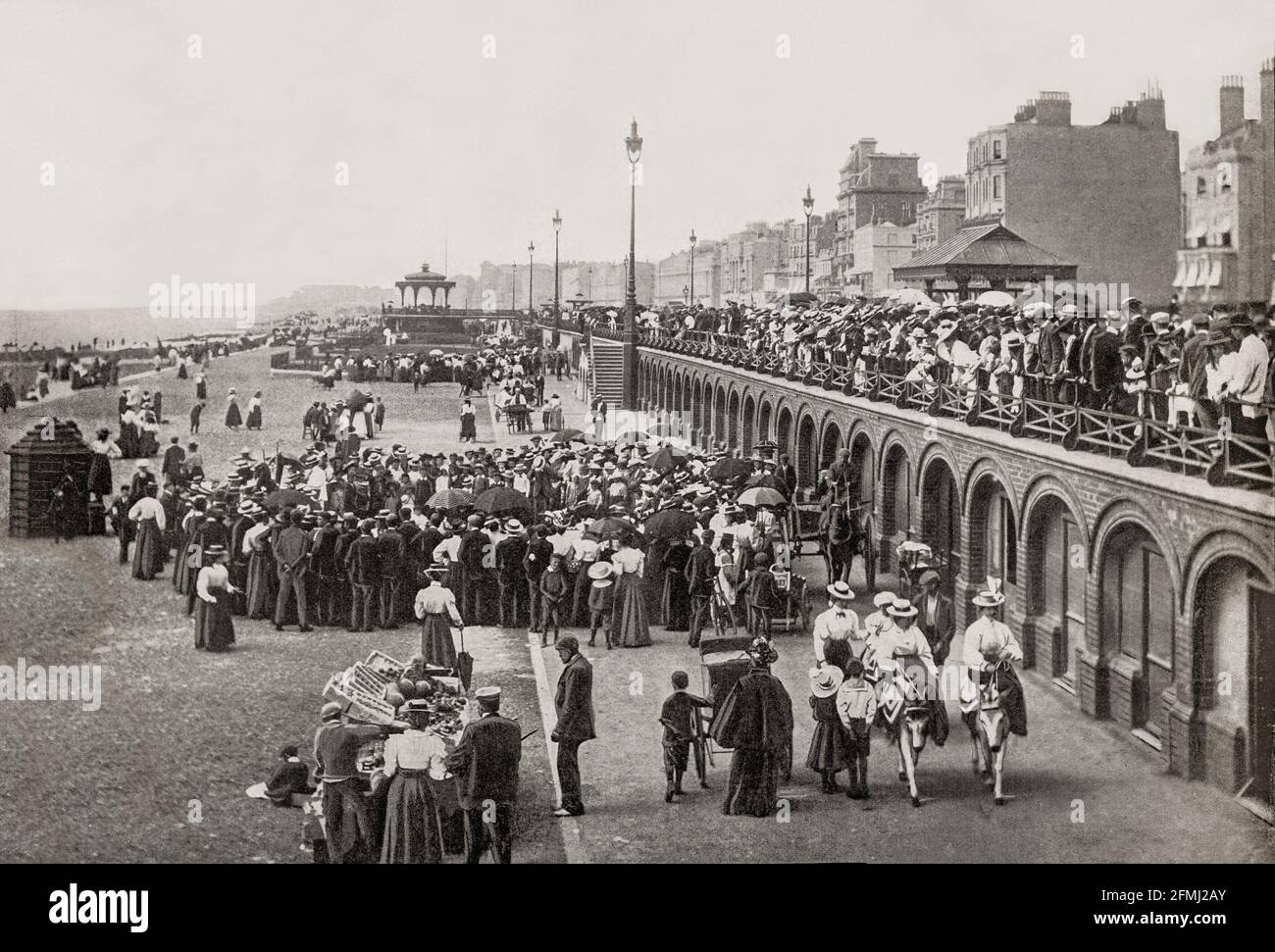 A late 19th Century view of the seafront at Brighton in East Sussex, England. King George IV spent much time in the town and constructed the Royal Pavilion there. The arrival of the London and Brighton Railway in 1841 brought Brighton within the reach of day-trippers from London. Many of the major attractions were built during the Victorian era, such as the Grand Hotel (1864), the West Pier (1866), and the Palace Pier (1899). Stock Photo