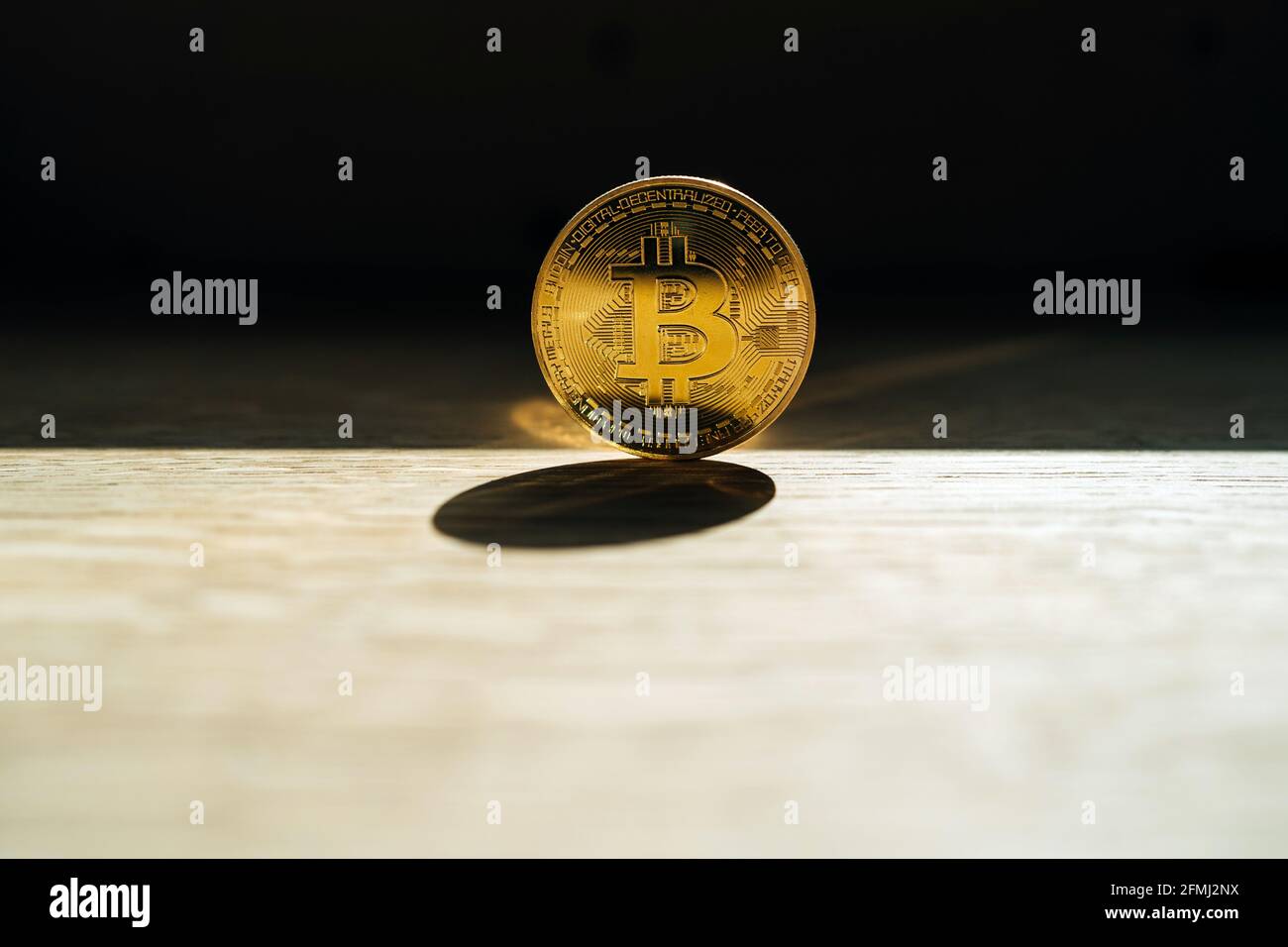 Metal coin with ornament and letter representing cryptocurrency symbol on desk with shade on dark background Stock Photo