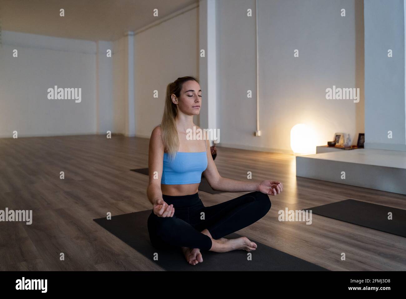 Peaceful slim female sitting on mat in Lotus pose and meditating with ...